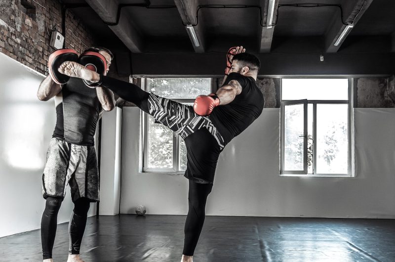 Male fighter training kicks with partner with training boxing paws